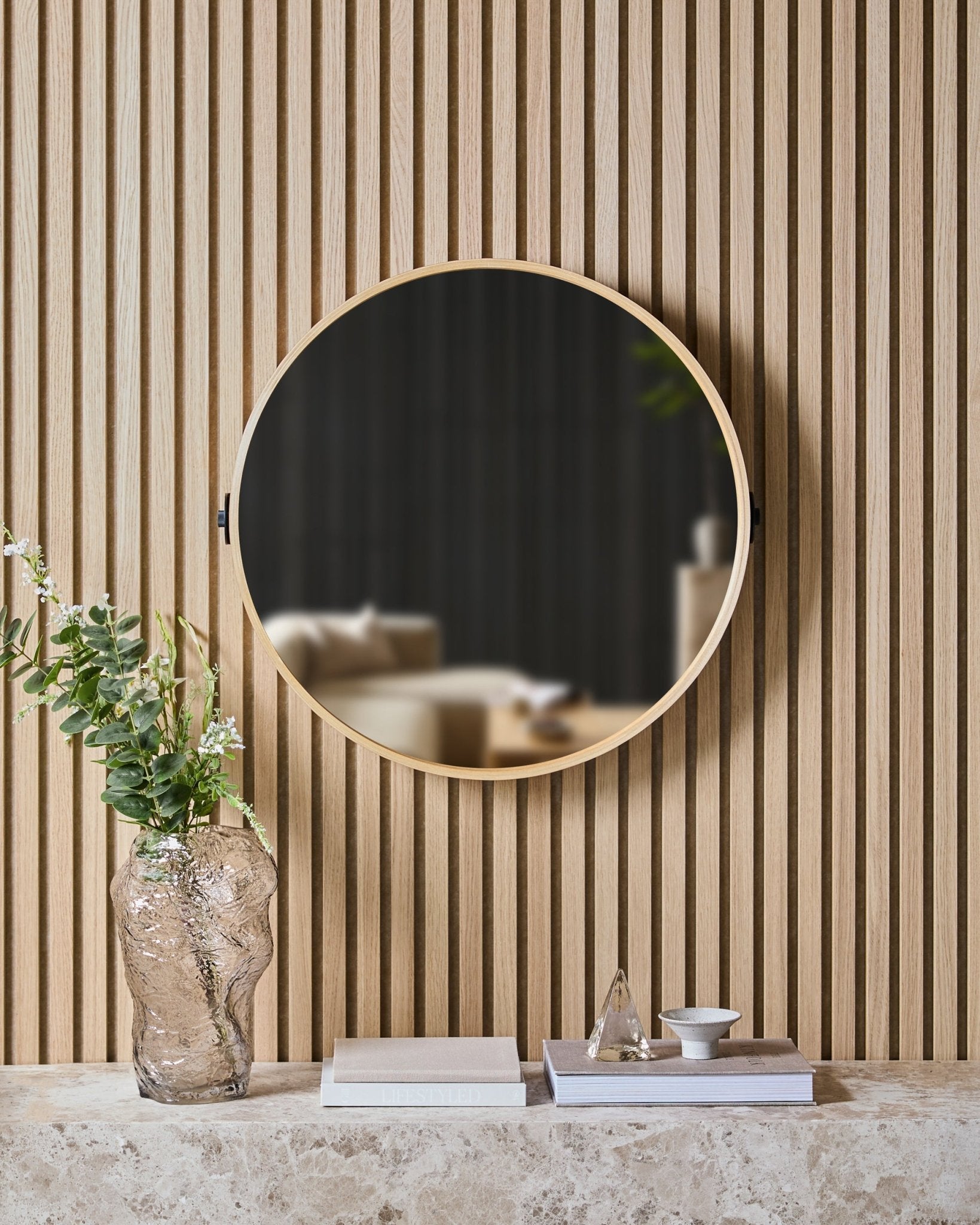 Der Linn | Mirror in Natural Oak von WoodUpp ist an einer nordischen Akustikpaneel-Wand Akustikpaneel über einem Steinregal mit Glasvase, Büchern und Dekoobjekten montiert.